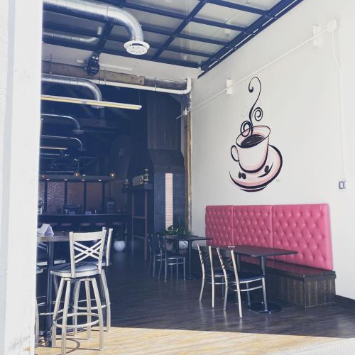 A cozy café interior featuring pink tufted seating, wooden tables, and a coffee cup mural on the wall.