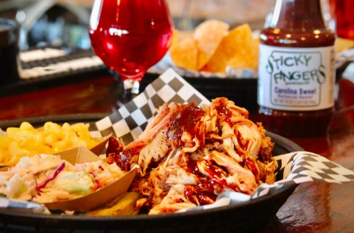 A plate of pulled pork with barbecue sauce, macaroni and cheese, coleslaw, and a bottle of Sticky Fingers sauce.