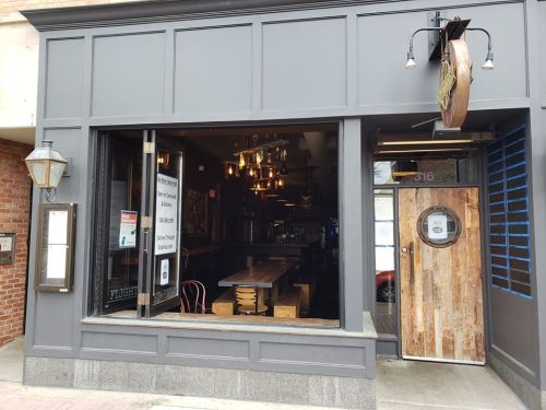 Exterior view of a restaurant with large windows, wooden door, and a rustic sign, showcasing a cozy interior.