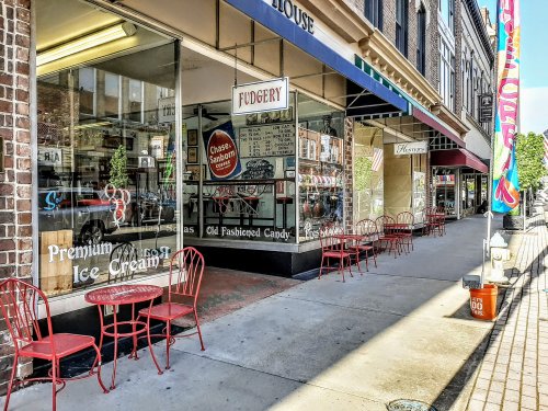 A charming street scene featuring a candy shop and ice cream parlor with red outdoor seating and storefronts.