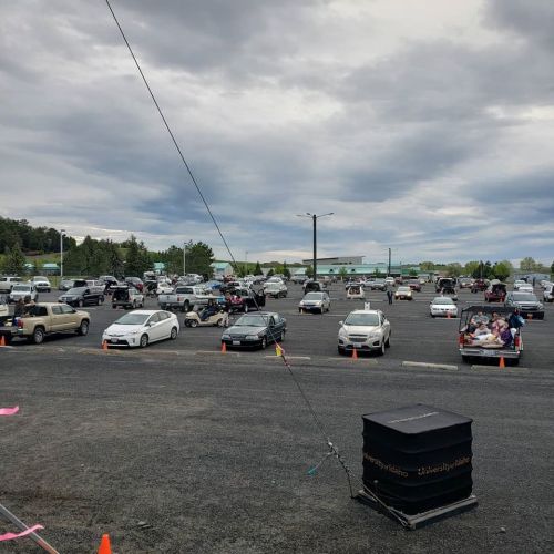 A crowded parking lot filled with cars, some with people inside, under a cloudy sky.