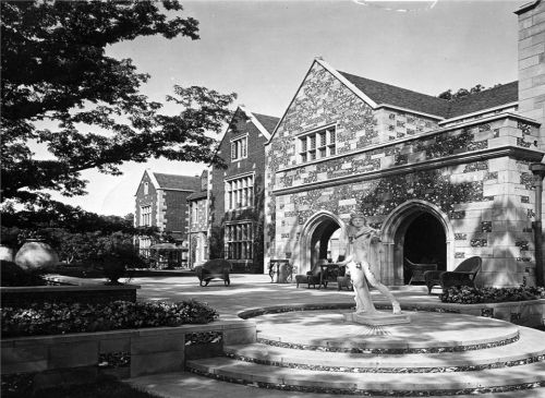 A historic stone mansion with intricate architecture, featuring a statue and outdoor seating in a landscaped area.