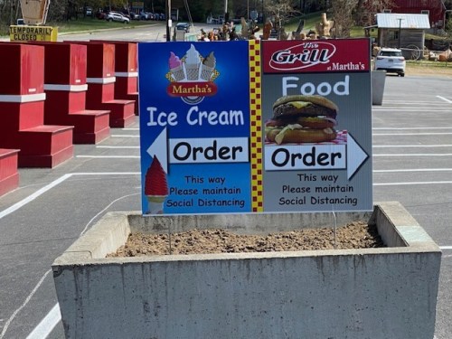 Two signs directing customers to order ice cream and food, with arrows and reminders for social distancing.