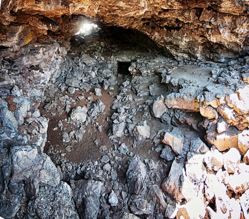 A rocky cave interior with scattered stones and a small opening allowing light to enter.