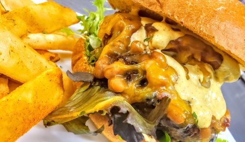 A close-up of a juicy burger with melted cheese, lettuce, and sauce, served with crispy fries on the side.