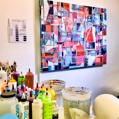 A colorful abstract painting hangs on a wall above a table with various paint containers and tools.