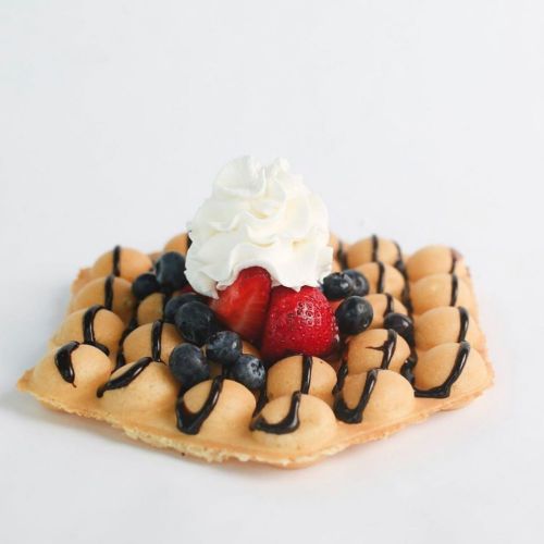 A golden waffle topped with whipped cream, strawberries, blueberries, and drizzled with chocolate sauce.