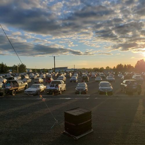 A large parking lot filled with cars at sunset, with clouds in the sky and a few trees in the background.