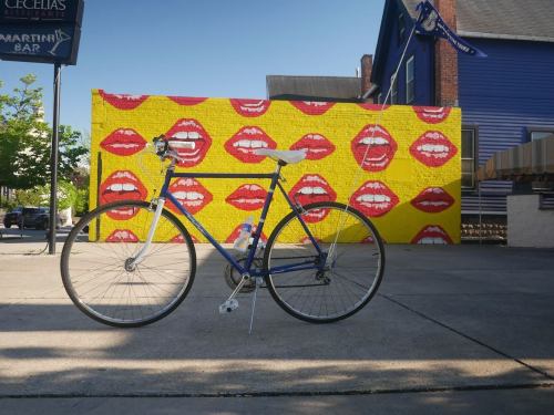 A blue bicycle parked in front of a vibrant yellow wall featuring red lips and smiling faces.