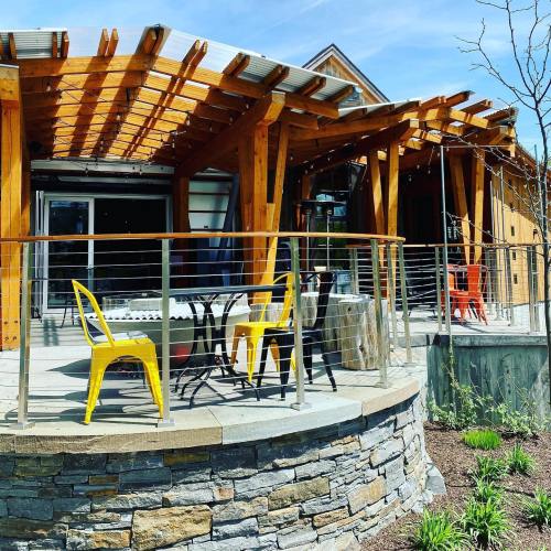 A modern outdoor patio with wooden beams, stone walls, and colorful chairs around a table on a sunny day.