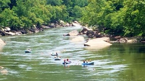 A serene river scene with people in inflatable rafts surrounded by lush greenery and large rocks.