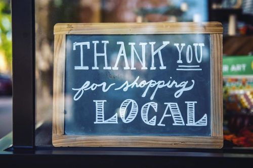 Chalkboard sign reading "Thank You for Shopping Local" with a wooden frame, displayed in a shop window.