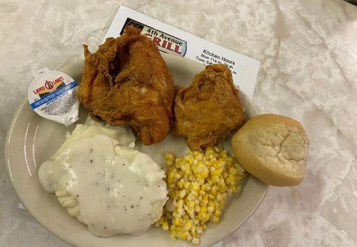 A plate with fried chicken, mashed potatoes with gravy, corn, and a roll on a table.