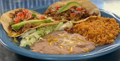 A blue plate with three tacos filled with meat, lettuce, and tomatoes, served with rice and refried beans.