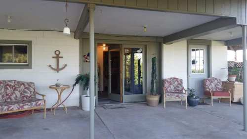 A cozy porch with two chairs, a small table, and plants, leading to an entrance with a welcoming interior.