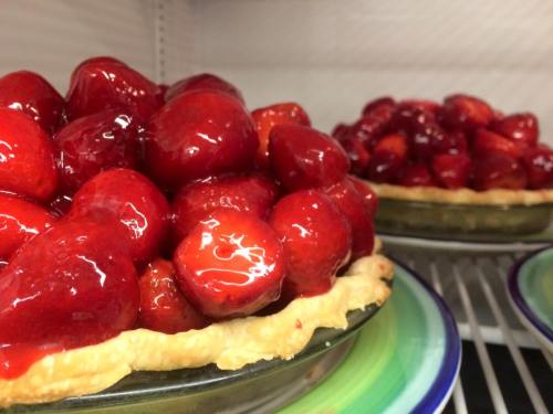 Two strawberry pies with glossy red fruit topping on a flaky crust, displayed on colorful plates.