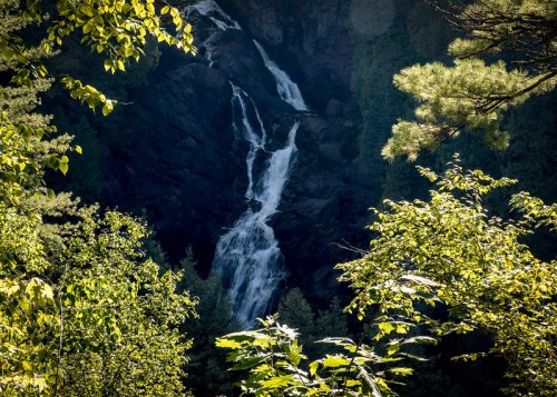 A cascading waterfall surrounded by lush green trees and rocky cliffs in a serene natural setting.