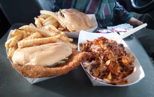 A meal featuring a fried chicken sandwich, two burgers, and a large serving of crinkle-cut fries on a table.