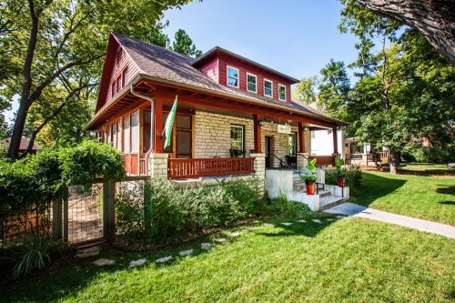 A charming two-story house with a red and stone exterior, surrounded by greenery and a well-maintained lawn.