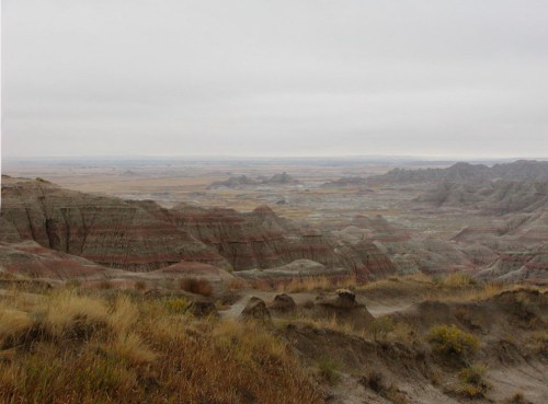 A vast, rugged landscape with layered rock formations and sparse vegetation under a cloudy sky.