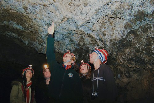 A group of five people in helmets with headlamps, exploring a cave and looking up at the rocky ceiling.