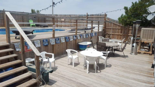 A wooden deck with a pool, chairs, tables, and decorations, set up for a casual outdoor gathering.