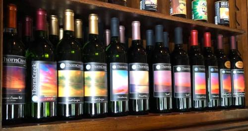 A wooden shelf displaying various bottles of ThornCreek wine, each with colorful sunset-themed labels.