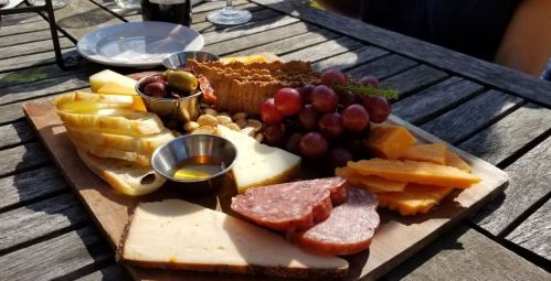 A wooden platter with assorted cheeses, meats, olives, grapes, nuts, and honey, set on a rustic table.