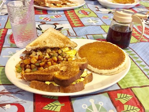 A plate of breakfast featuring a sandwich with eggs and potatoes, a pancake, and a glass of water with a straw.