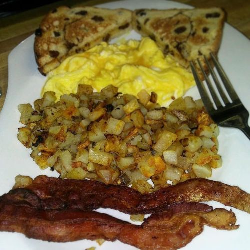 A plate with chocolate chip pancakes, scrambled eggs, crispy bacon, and golden-brown hash browns.