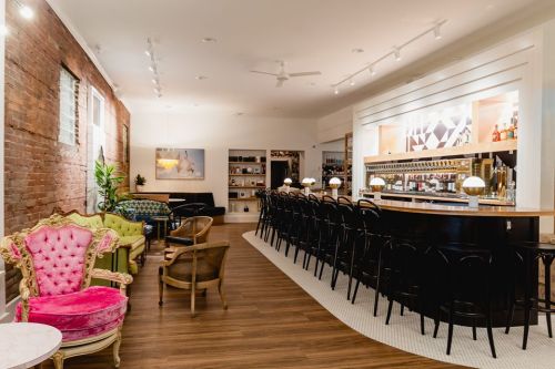 A stylish bar interior featuring a long counter, colorful seating, and warm lighting in a modern space.