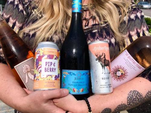 A person holds five bottles of wine and beer, showcasing a variety of colorful labels and styles.