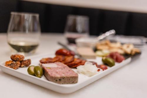 A platter of assorted meats, cheeses, olives, and snacks, with glasses of wine in the background.