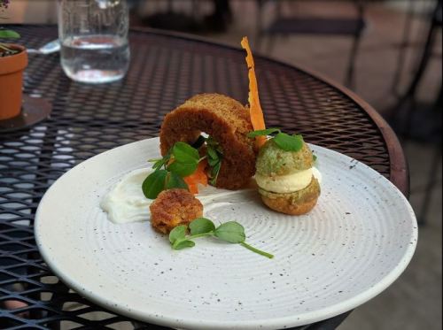 A plate with a circular cake, a small green patty, and a scoop of ice cream, garnished with greens and a carrot strip.