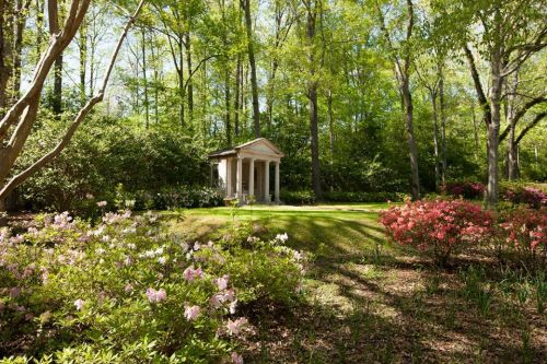 A serene garden with blooming azaleas and a classical gazebo surrounded by lush green trees.