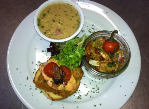 A plate featuring a bowl of soup, a salad, a slice of bread topped with tomatoes, and a jar of mixed vegetables.