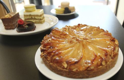 A variety of desserts on a table, including a glazed apple tart, layered cake, and assorted pastries.