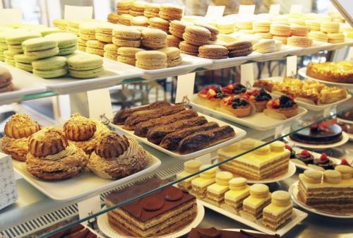 A display case filled with an assortment of colorful macarons, pastries, and layered cakes.