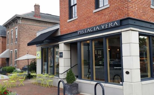 Exterior of Pistacia Vera, a brick building with large windows, outdoor seating, and a modern awning.