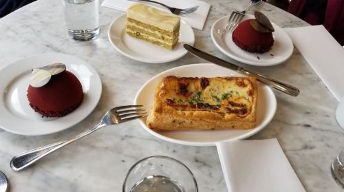 A marble table with three desserts and a savory pastry, accompanied by glasses of water and utensils.