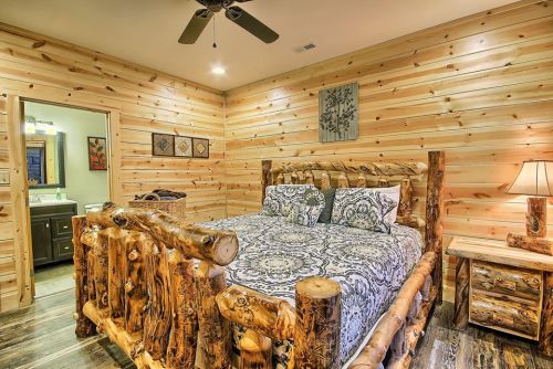 Cozy bedroom with a log bed, patterned bedding, wooden walls, and rustic decor. Soft lighting enhances the warm atmosphere.