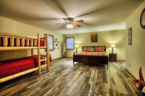 Cozy bedroom featuring a bunk bed, a queen bed, wooden floors, and warm lighting.