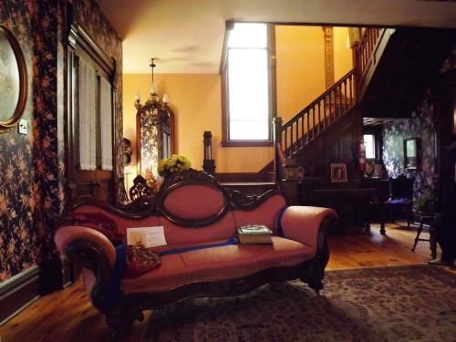 A vintage living room featuring a pink ornate sofa, floral wallpaper, and a staircase in the background.