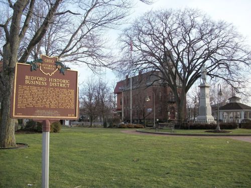 Sign for Bedford Historic Business District in Ohio, with a park, trees, and a gazebo in the background.