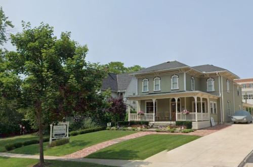 A charming historic house with a porch, surrounded by greenery, featuring a sign indicating it is a museum.