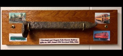 A wooden plaque displays a railway spike with images of vintage trains and a label about the Cleveland and Chagrin Falls Railway.