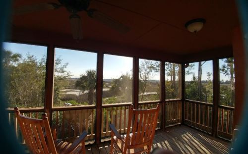 A screened porch with two rocking chairs overlooks a scenic view of trees and a distant landscape at sunset.