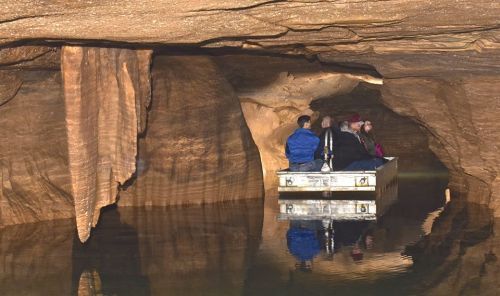 A group of people on a small boat inside a cave, surrounded by rock formations and calm water reflections.
