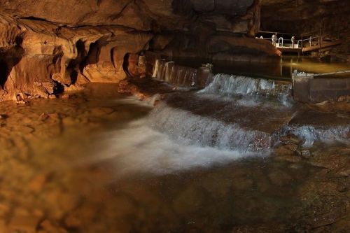 A serene underground cave with a small waterfall flowing into a calm pool of water, illuminated by soft lighting.