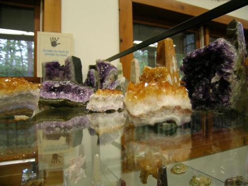 A display of various colorful crystals, including amethyst and citrine, reflecting on a glass surface.